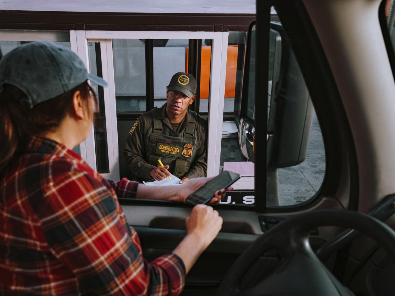 Truck driver talking to border control agent and referencing the Uber Freight carrier app on their phone